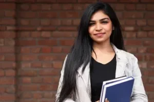 Joven con libros frente a un muro de ladrillo
