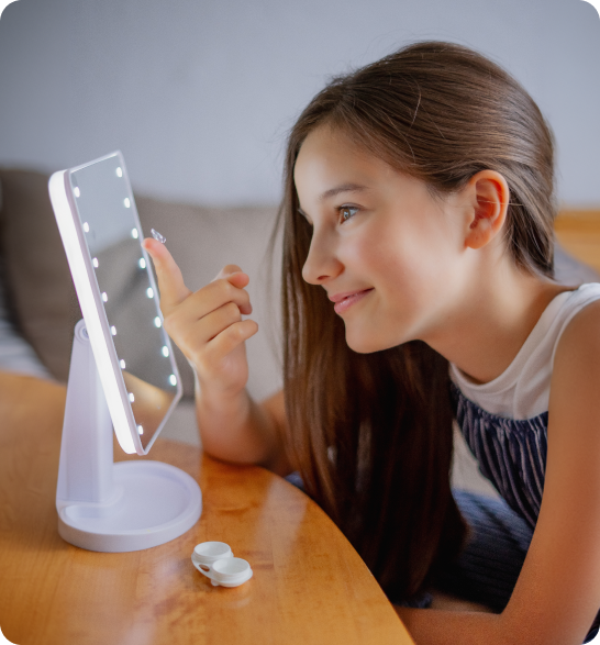 Niña colocándose un lente de contacto frente a un espejo con luz