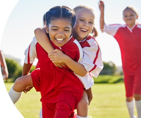 Dos niñas con uniforme de fútbol abrazadas y riendo en la cancha