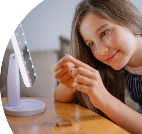 Niña colocándose un lente de contacto frente a un espejo con luz